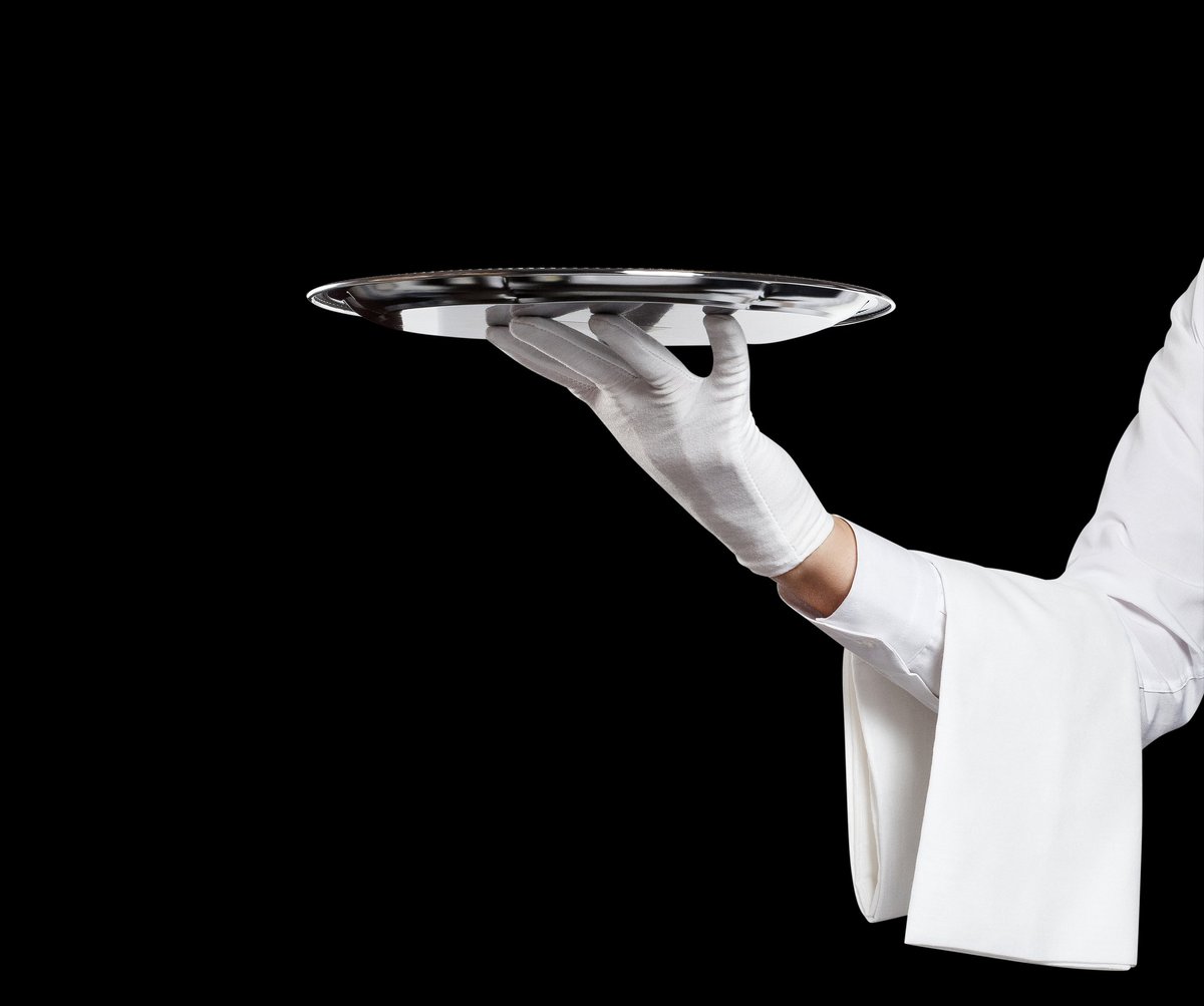 A white-gloved hand presenting a silver tray — the standard of care behind every itinerary