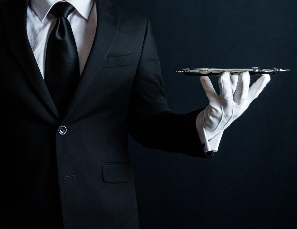 A butler in an immaculate suit and white gloves holding a silver tray