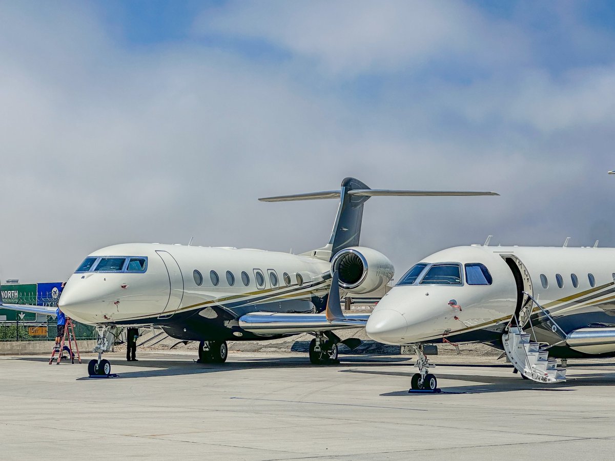 Two white, blue, and gold private jets parked on a runway, ready for departure