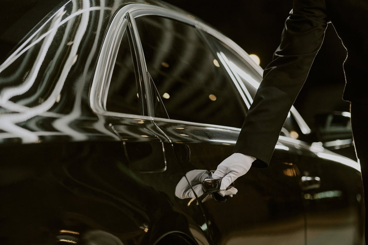 A chauffeur's hand opening the rear door of a luxury vehicle at night
