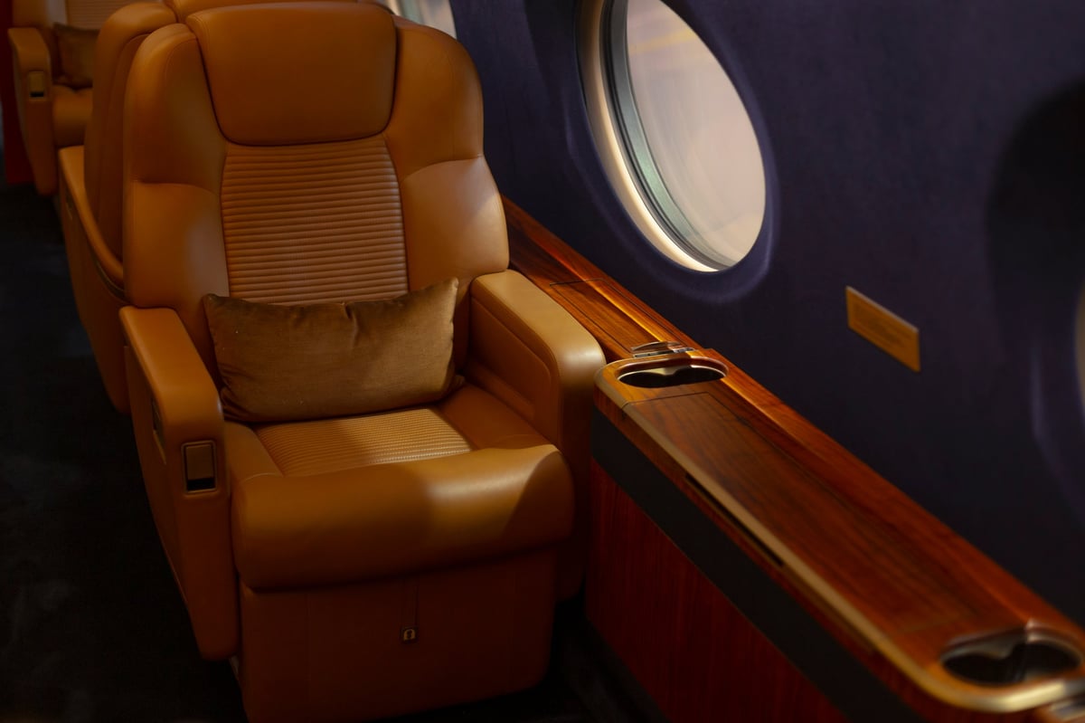 An opulent private jet interior with leather cabin, plush window-side seat, and soft lighting