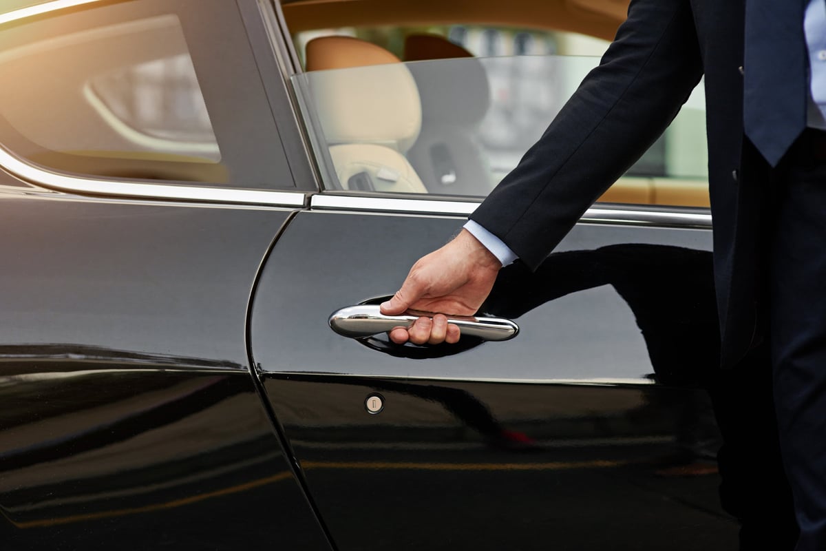 A gloved chauffeur opening a car door — the single point of contact attending to every detail