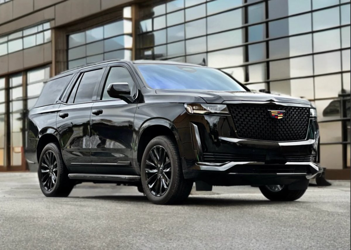 Black Cadillac Escalade SUV parked in front of modern glass building with industrial backdrop